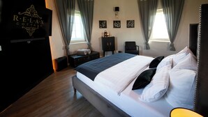A well-lit bedroom with a large bed, two windows with curtains, a side table, a chair, and a wall-mounted TV. - Eiffel Tower Suite / Water Tower (Utscheid)