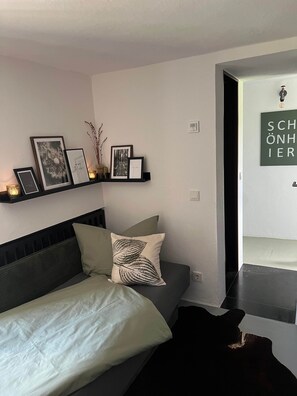 Ein Schlafzimmer mit einem Bett, einem Nachttisch, einem Regal mit gerahmten Bildern und einer Wandleuchte.