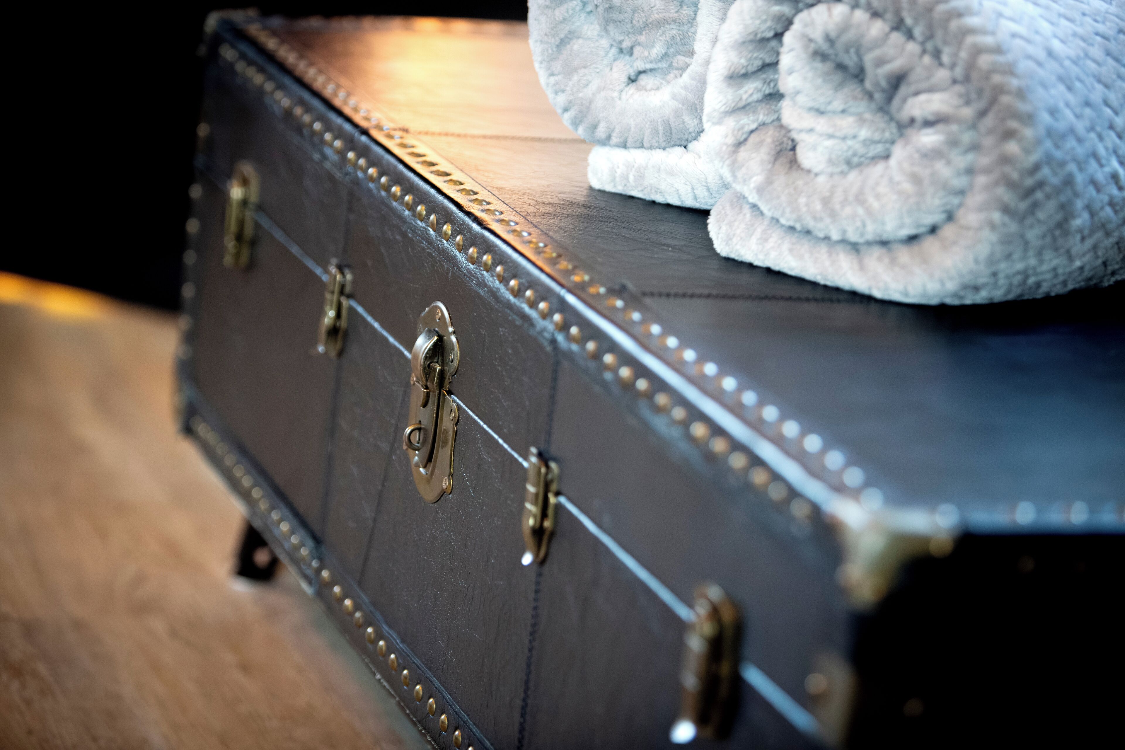 A dark brown suitcase with brass clasps and rivets, placed on a wooden surface.