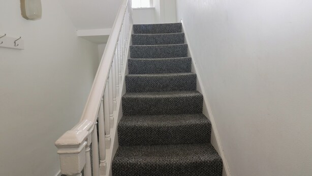 Un escalier avec une rampe blanche et des marches recouvertes de moquette.