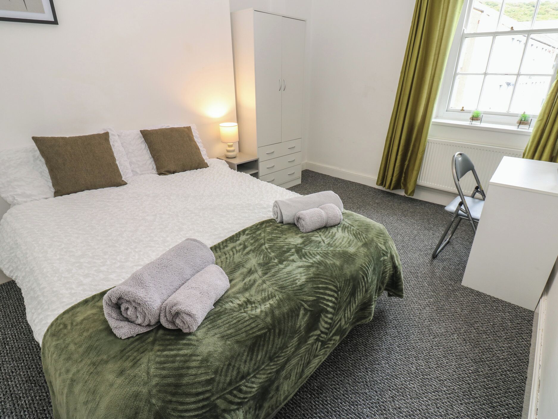 Een hotelkamer met een bed, een bureau, een stoel, een kledingkast en een raam met gordijnen.