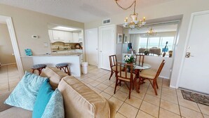 A spacious living area with a sofa, dining table, and chairs, a kitchen with white cabinets, and a view of the balcony. - Crescent Arms Vacation Rentals 501S Siesta Key Florida (Sarasota)
