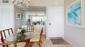 A dining area with a glass table and wooden chairs, a chandelier, and a framed painting on the wall. - Crescent Arms Vacation Rentals 501S Siesta Key Florida (Sarasota)