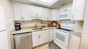 A compact kitchen with white cabinets, a built-in dishwasher, a stove, and a microwave. - Crescent Arms Vacation Rentals 501S Siesta Key Florida (Sarasota)