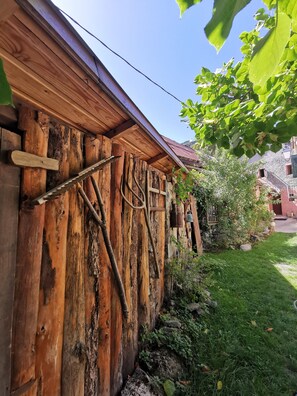 A rustic wooden wall with a metal ladder and pipes, a stone building in the background, and a well-maintained grassy area. - SARL SCOP BIENVENUE A L AUBERGE  (Sauze)