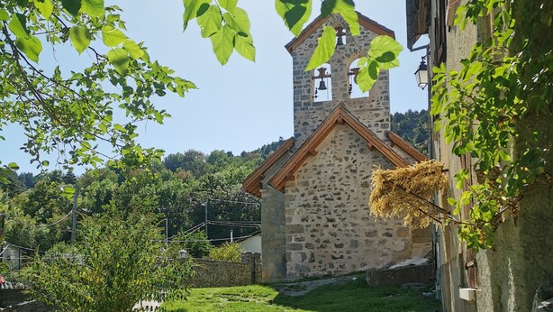 Una iglesia de piedra con un campanario, rodeada de césped y árboles.