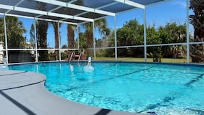 A swimming pool with a covered area, surrounded by palm trees and greenery. - Charming 2-bedroom house in lovely New Port Richey with pool. (New Port Richey)