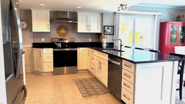 A modern kitchen with white cabinets, stainless steel appliances, and a large island. - Charming 2-bedroom house in lovely New Port Richey with pool. (New Port Richey)