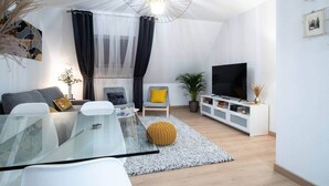 A modern living room with a glass coffee table, a sofa, a chair, a TV, and a white entertainment unit. - Superb apartment in the heart of Colmar (Colmar)