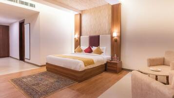 A modern hotel room with a large bed, a wooden headboard, bedside lamps, a small table, and a chair.