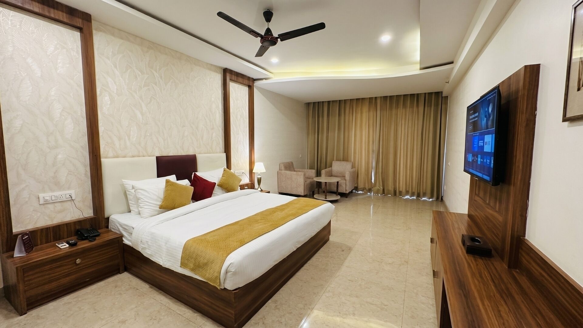 A hotel room with a bed, bedside tables, a TV, a ceiling fan, and a view of the outside.