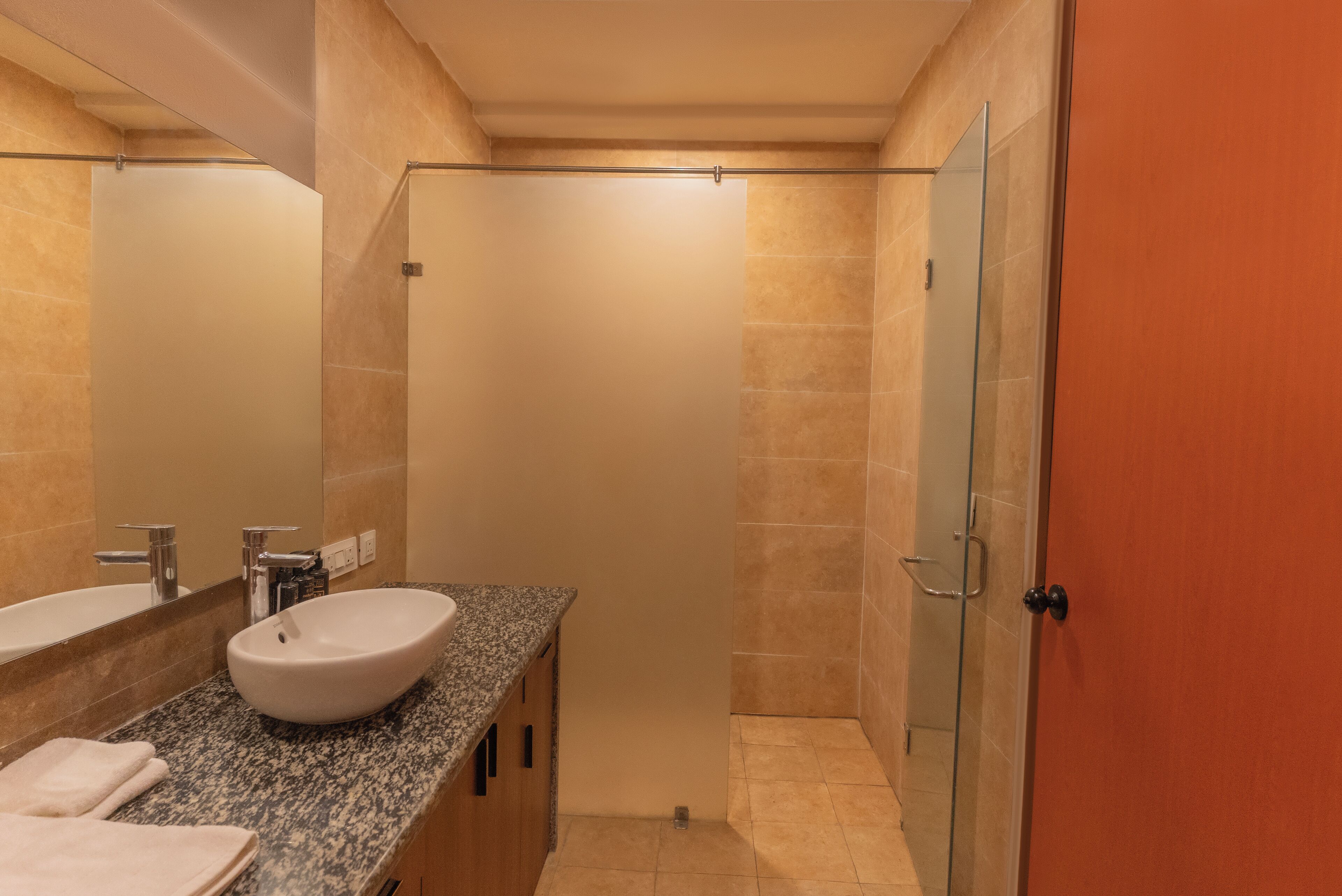 A modern bathroom with a granite countertop, a white sink, and a glass shower enclosure.