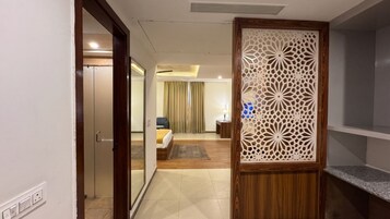 Habitación de hotel con cama, escritorio, silla, separador decorativo y vista al pasillo.