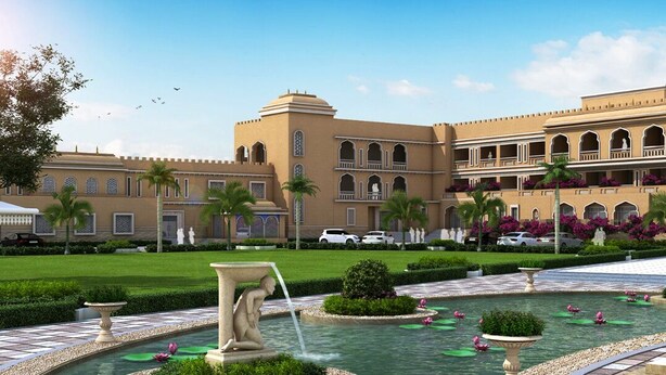 A courtyard with a fountain, palm trees, and a building with arched windows and balconies. - Haut Monde Rajputana Palace (Behror)