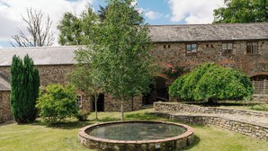 Ein Steinhaus mit einem runden Pool, umgeben von Gras und Bäumen.