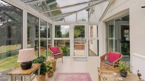 Ein Wintergarten mit Glastüren, Korbmöbeln, einem Tisch mit Lampe und Topfpflanzen.