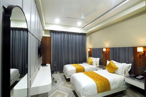A hotel room with two beds, a desk, a mirror, a ceiling fan, and a large window with curtains. - Hotel Breeze Bay ex (Mumbai)