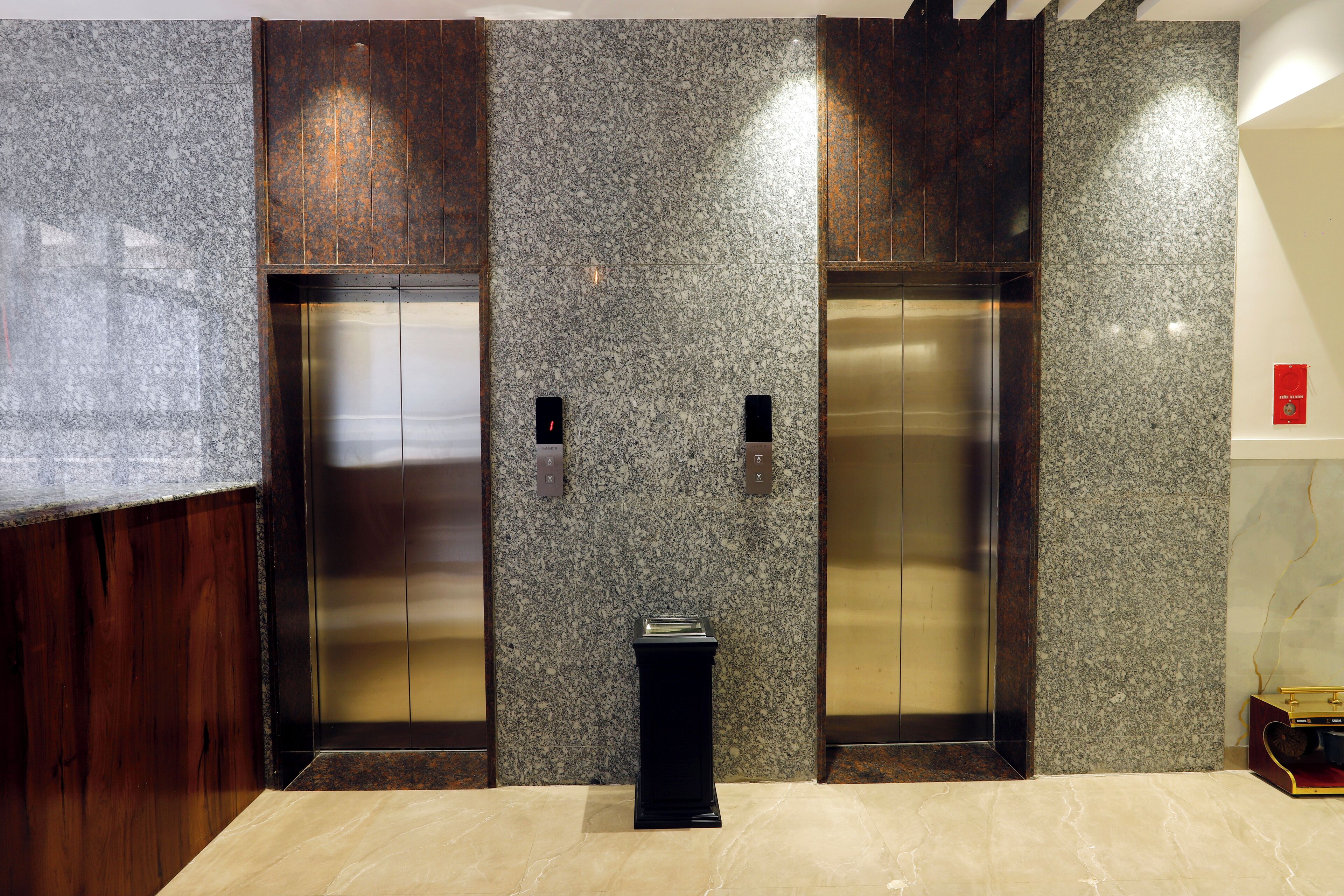 A modern elevator with metallic doors and a control panel in a lobby with marble flooring and wooden paneling.