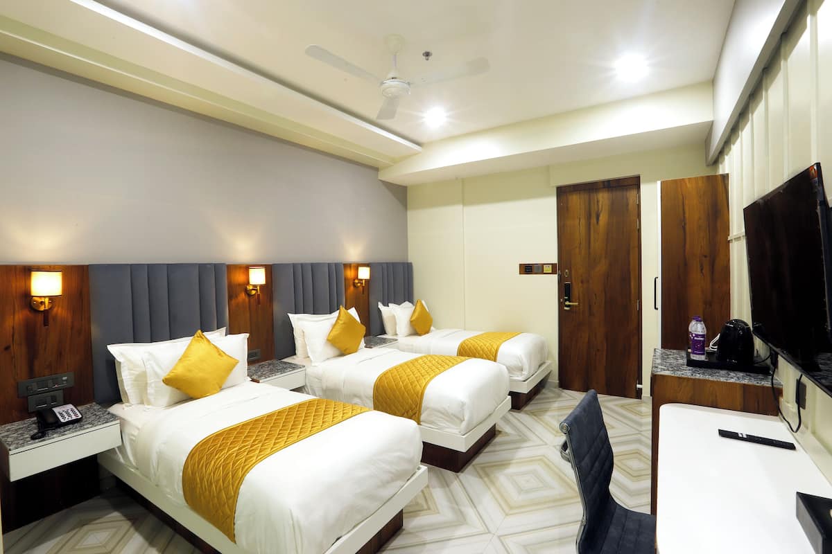 A hotel room with three beds, a desk, a TV, and a ceiling fan.