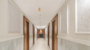 A long, narrow hallway with marble flooring and wooden doors on both sides. - Hotel Breeze Bay ex (Mumbai)