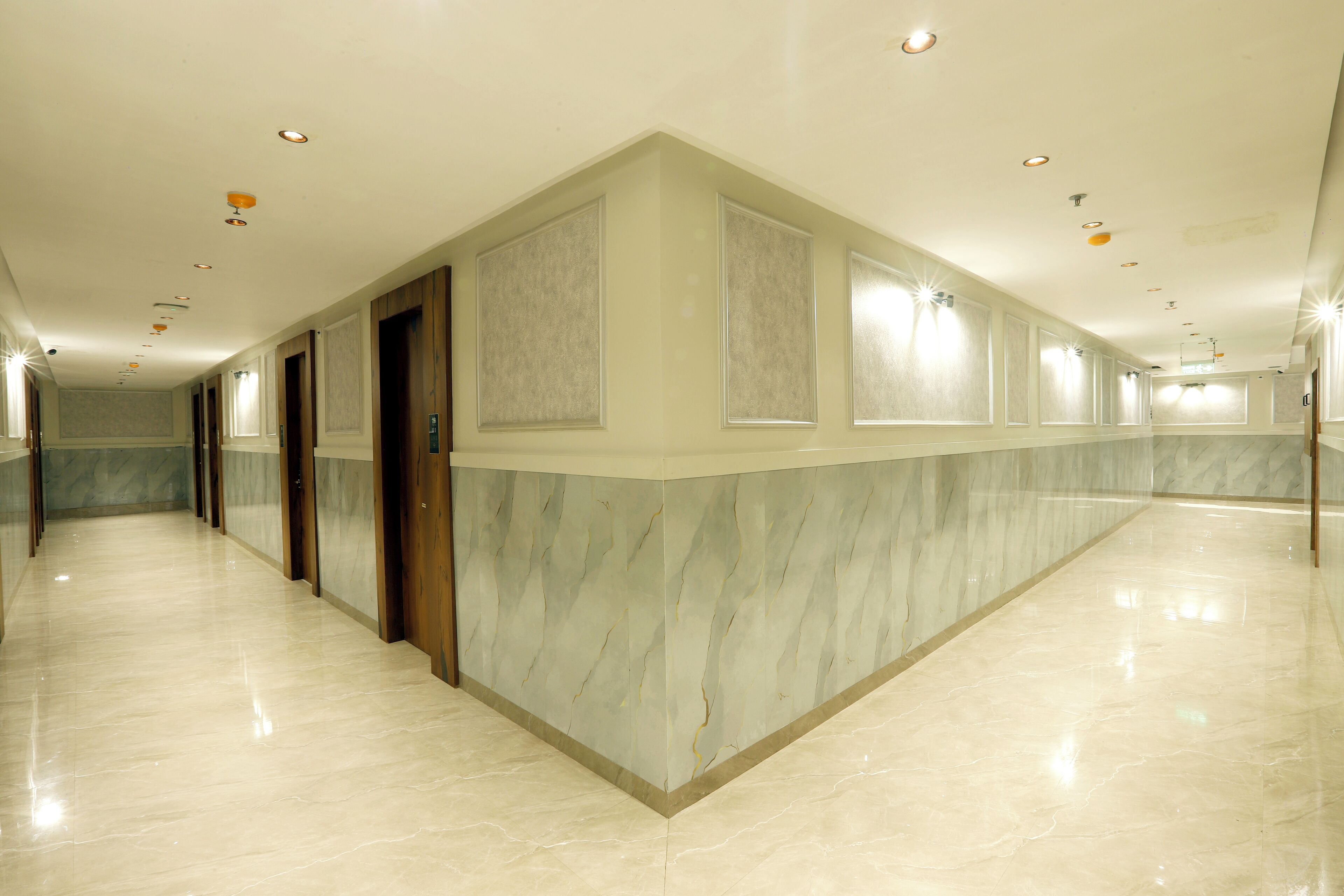 A long, well-lit corridor with marble walls and doors, leading to multiple rooms.