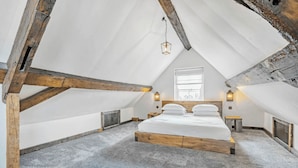 A bedroom with a sloped ceiling, exposed wooden beams, a large bed, a window, and wall-mounted lights. - Chester Rose, Chester (Chester)