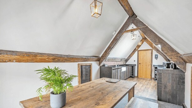 A cozy attic room with a wooden dining table, a potted plant, and a kitchen area with wooden cabinets. - Chester Rose, Chester (Chester)