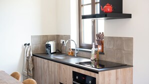 Una cucina moderna con un piano di lavoro nero, mobili in legno, forno integrato, lavello e una finestra con una pentola rossa sullo scaffale sopra.
