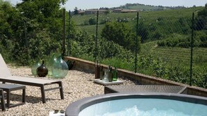 Una vasca idromassaggio con vista su un vigneto, circondata da una recinzione e con area salotto esterna.