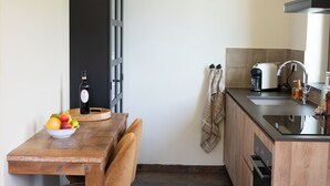 Una cucina con un tavolo di legno, una ciotola di frutta, una bottiglia di vino e una macchina per il caffè.