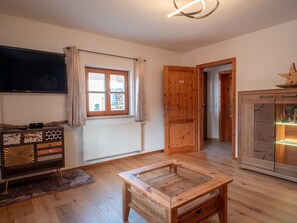 Quarto com piso de madeira, televisão, janela com cortinas, porta de madeira e armário com luz.