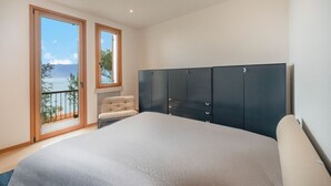 Un dormitorio con una cama grande, un armario, una silla y un balcón con vistas al mar.