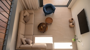 Una sala de estar moderna con un sofá modular, un sillón azul, dos mesitas de madera y una planta en maceta.