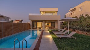 Una casa moderna de dos pisos con piscina, mobiliario exterior y un jardín bien cuidado.