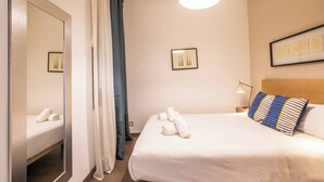 A hotel room with a bed, a mirror, a nightstand, a lamp, and two framed pictures on the wall.