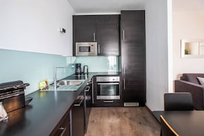 A compact kitchen with dark cabinetry, a stainless steel sink, a microwave, and an oven.