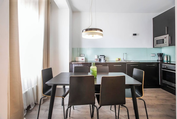 A modern kitchen with a dining area, featuring a table with chairs, a hanging light fixture, and a microwave.