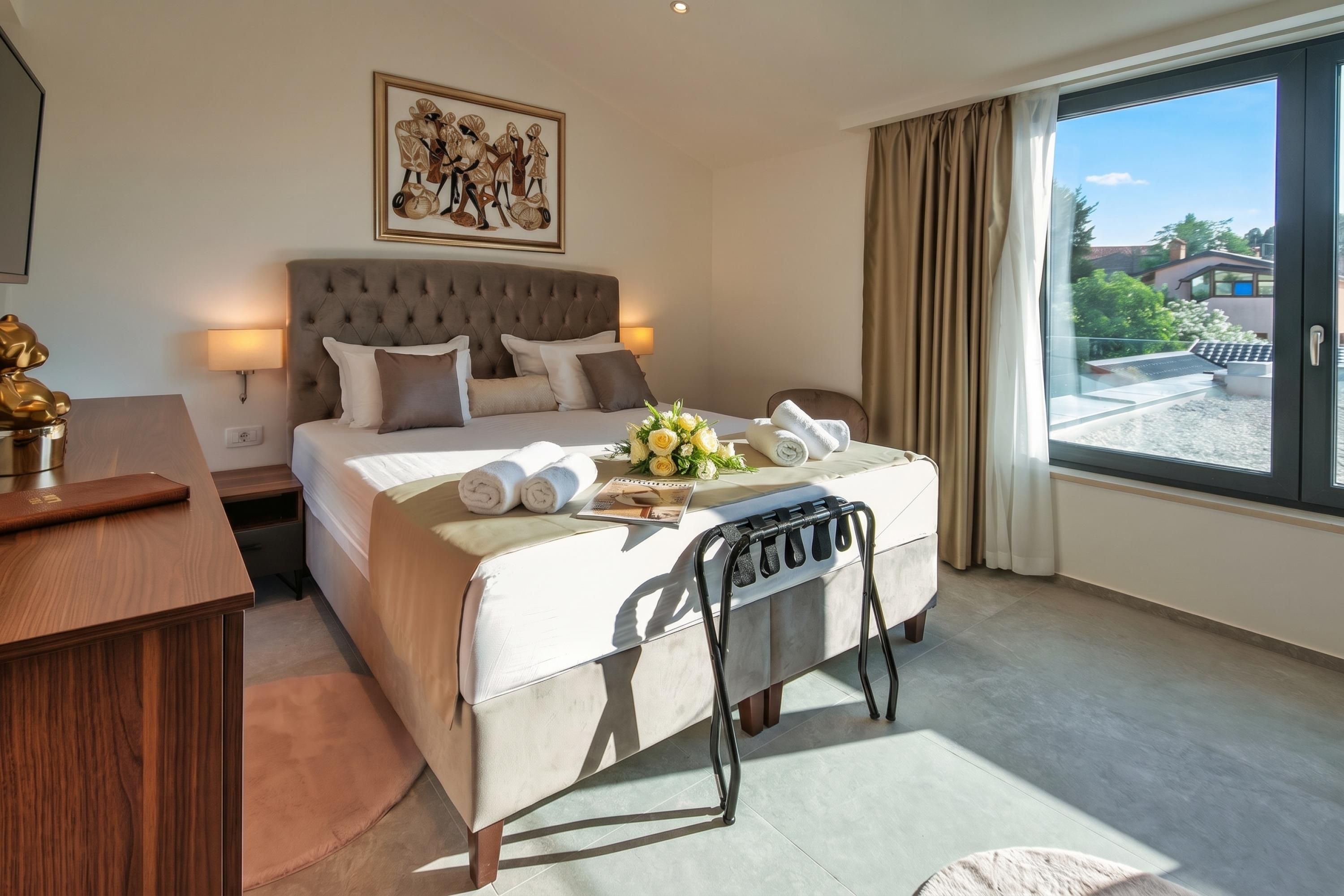 A hotel room with a large bed, a bedside table, a desk, a chair, a window with a view, and a painting on the wall.