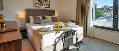 A hotel room with a large bed, a bedside table, a desk, a chair, a window with a view, and a painting on the wall.