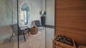 A modern interior with two black chairs, a round wooden table, a large mirror, a television on the wall, and a wooden bench with rocks. - Villa Kim Momjan With Pool and Spa (Buje)