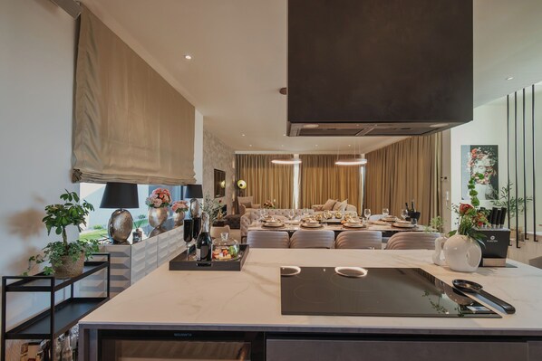 Una cocina moderna con una isla central, zona de comedor con sofá y un amplio ventanal con cortinas.