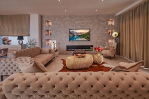 Een moderne woonkamer met een grote bank, een bijzettafeltje en een flatscreen televisie aan de muur.