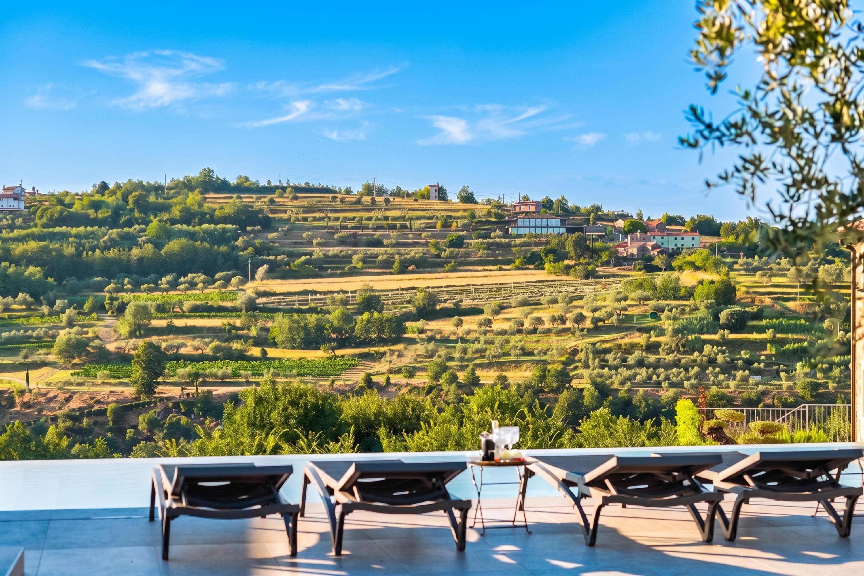A terrace with lounge chairs overlooking terraced vineyards and a village.