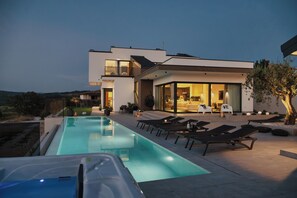 Una casa moderna con piscina, sillas de descanso y un interior bien iluminado.