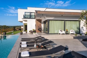 Een modern huis met een zwembad, ligbedden en uitzicht op het platteland.
