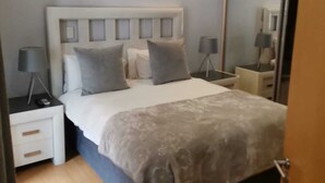 Un dormitorio con cama, mesitas de noche, un espejo y un aire acondicionado.