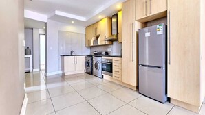 Una cocina moderna con armarios de madera clara, electrodomésticos de acero inoxidable y suelo de baldosas.