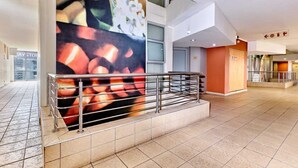 Un moderno vestíbulo de hotel con un gran mural abstracto, una escalera con barandilla de metal y una zona de cafetería.