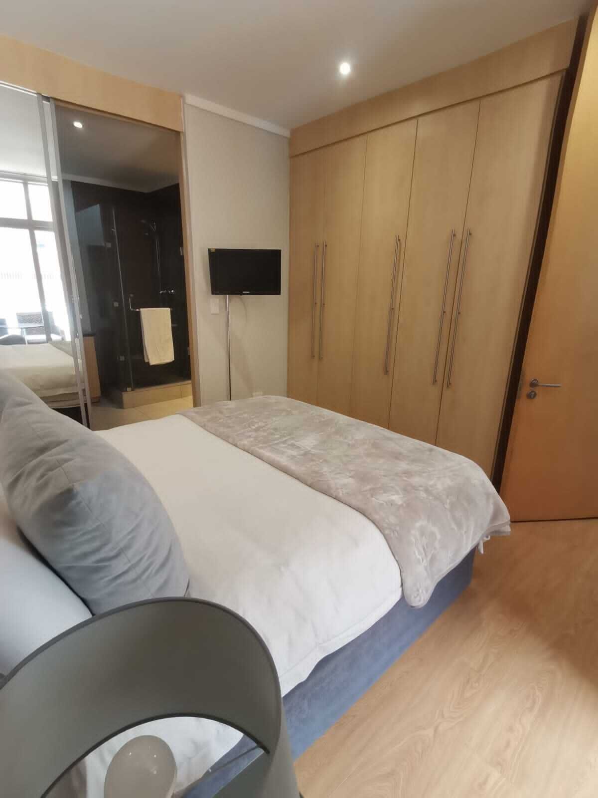 Ein Schlafzimmer mit Bett, Fernseher, Kleiderschrank und Duschbereich.