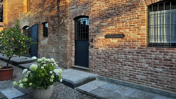 A brick building with a black door and windows, a small garden with white flowers, and a gravel pathway. - Podere Montevalle's Clubhouse (Provincia di Piacenza)
